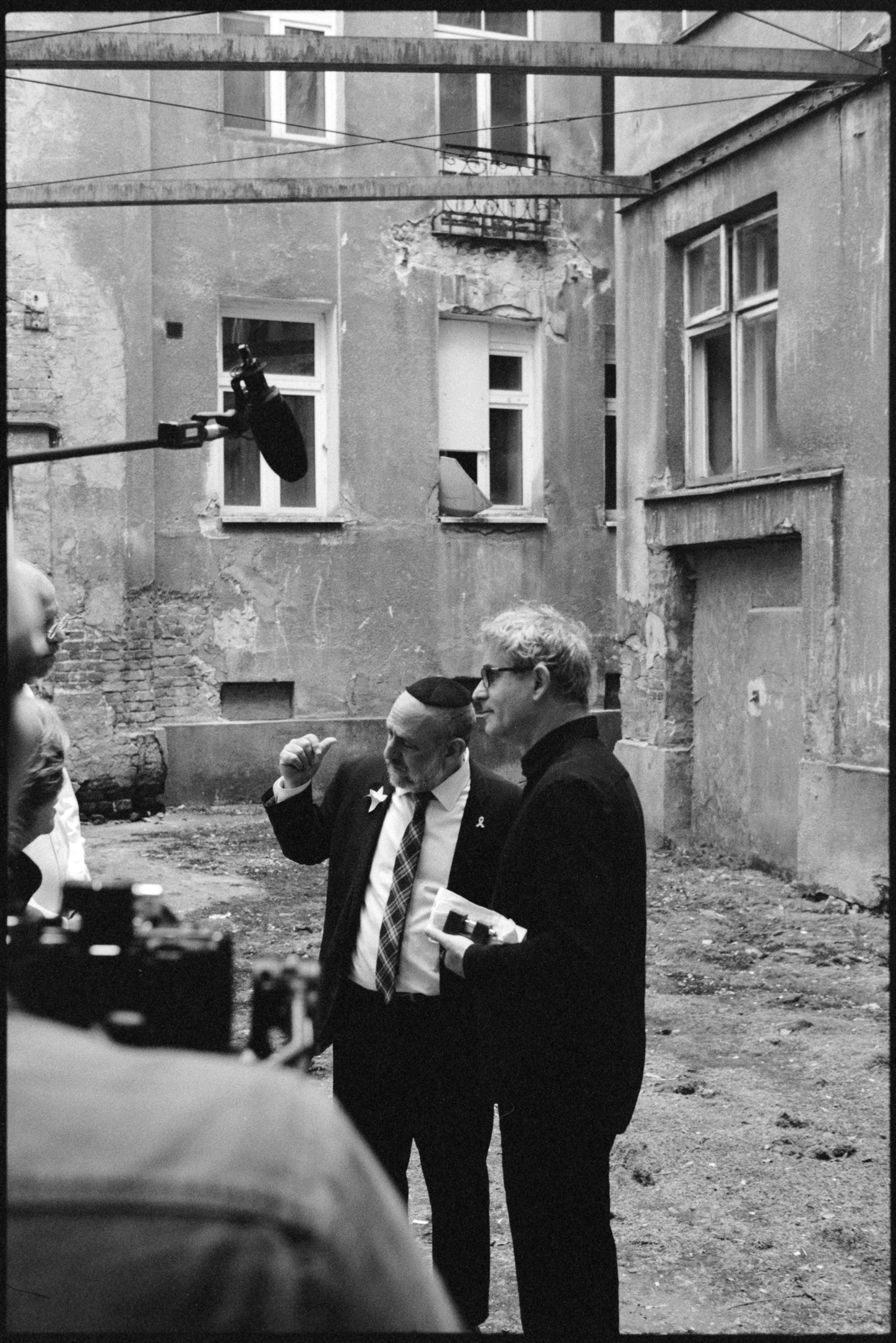 Seen past the boom microphone and camera, two men in conversation in the courtyard of an abandoned tenement.