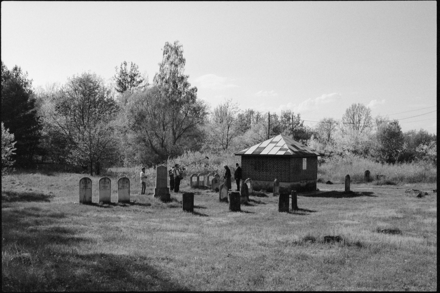 The crew films among the gravestones of the Jewish cemetery of Góra Kalwaria, the brick ohel behind them.