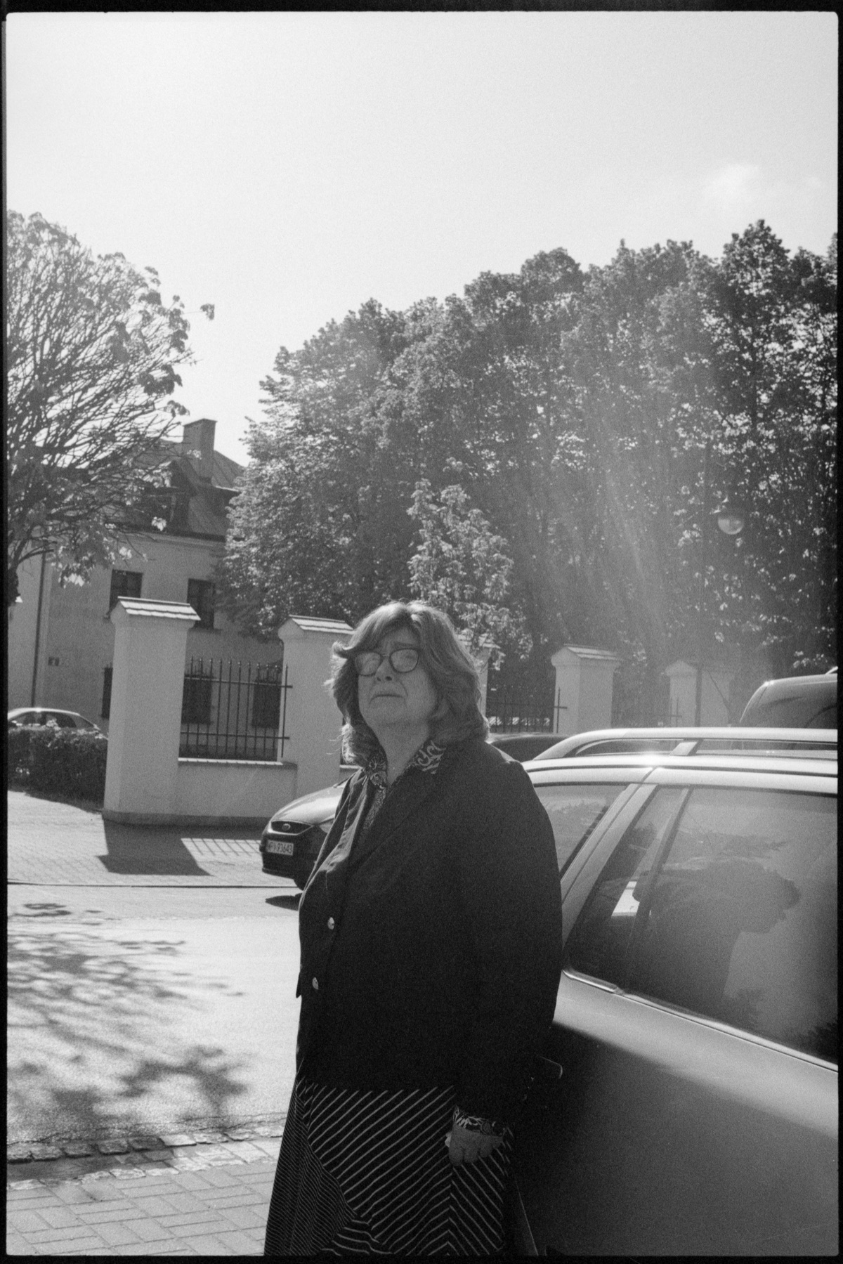 Dr. Ruth Lichtenstein stands beside a car in the sunlight, looking upward, mid-journey.